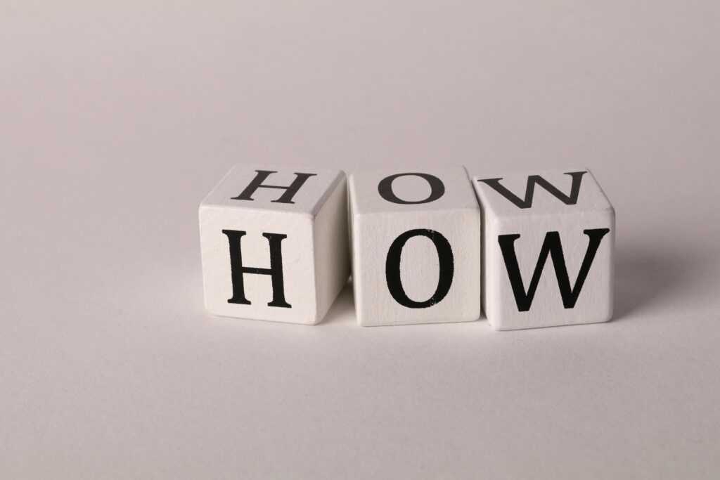 Close-up of white wooden cubes with the letters 'H', 'O', and 'W' arranged on a neutral background.