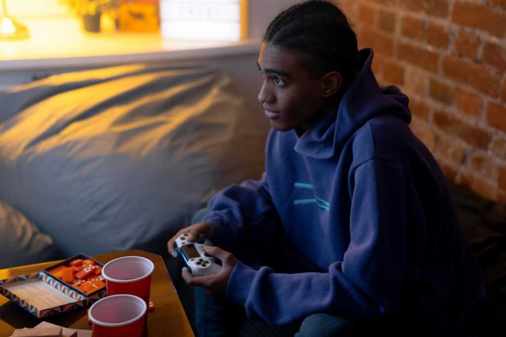 Teen focused on gaming indoors, holding a controller during a relaxed evening.
