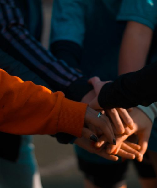 A close-up of diverse hands stacked together outdoors, symbolizing teamwork and unity.