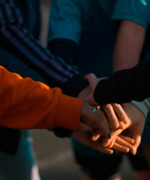 A close-up of diverse hands stacked together outdoors, symbolizing teamwork and unity.
