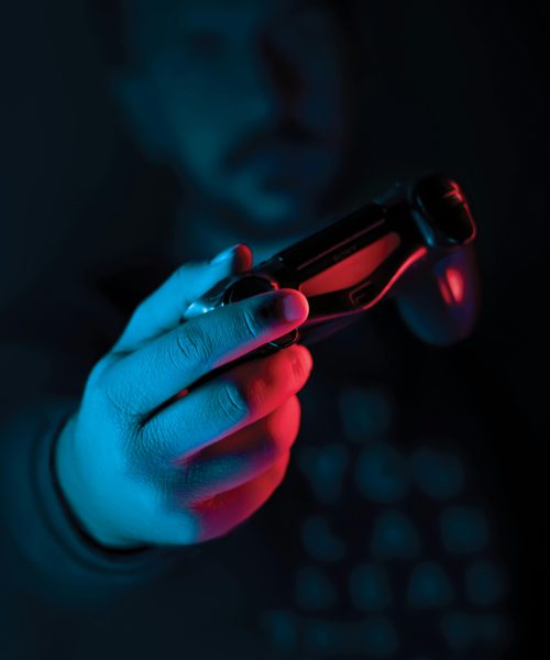 Close-up of a man's hand holding a joystick against a dark background with red and blue lighting.