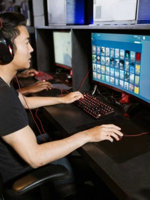Two young men play video games at a cyber cafe, showcasing modern gaming technology indoors.