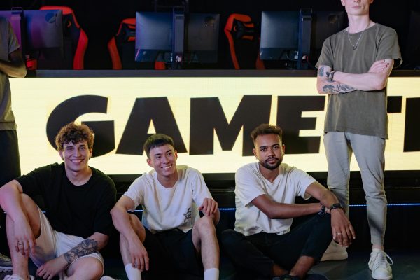 Four young men posing confidently in an eSports arena with gaming setups in the background.